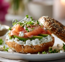 Cottage cheese protein bagel cut and topped with avocado and smoked salmon on a slate board.