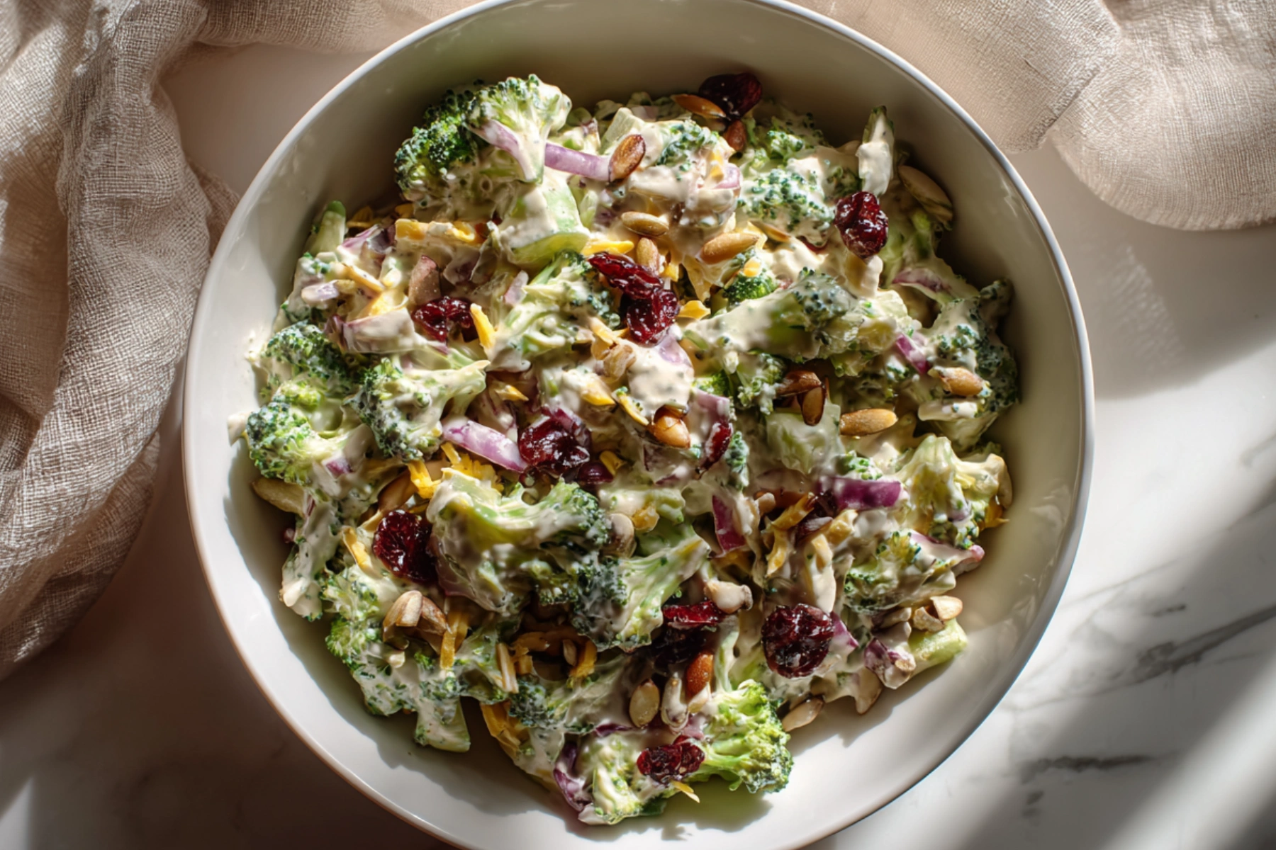 Creamy broccoli cheddar salad with cranberries red onion and sunflower seeds in a white bowl